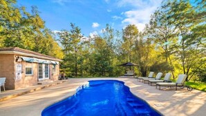 Una piscina con sillas de descanso y un pabellón en un área boscosa.