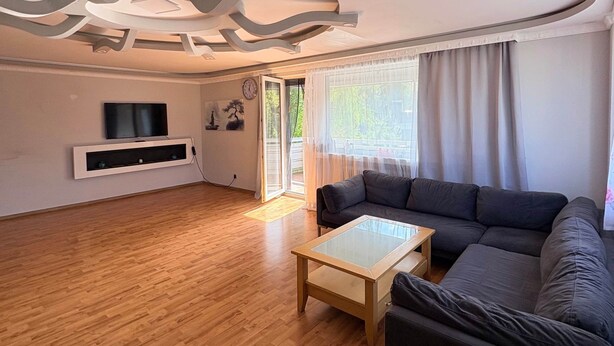 A modern living room with a wooden floor, a black sofa, a glass coffee table, and a TV mounted on the wall. - Spacious lodging near the industrial park (5 beds) (Bielefeld)