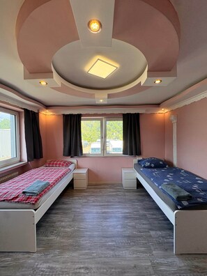 Une chambre avec deux lits, une fenêtre avec des rideaux, un luminaire au plafond et un radiateur.