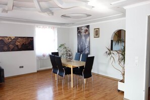 A dining area with a wooden table and chairs, a world map on the wall, and a large elephant painting.