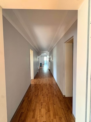 A long, narrow hallway with wooden flooring and white walls. - Spacious housing in a mixed-use area (Bielefeld)