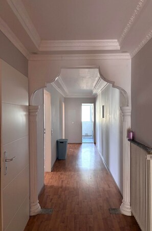 Un couloir avec un plancher en bois, des murs blancs et un radiateur sur le côté droit.