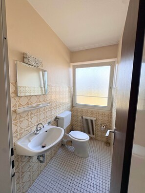 A bathroom with a toilet, sink, and window.