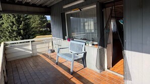 Un espace extérieur abrité, doté d’un sol en briques, d’un banc, d’une table et d’une fenêtre avec un rideau.