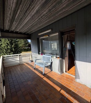 A covered outdoor area with a brick floor, a bench, a table, and a window with a curtain. - Spacious housing in a mixed-use area (Bielefeld)