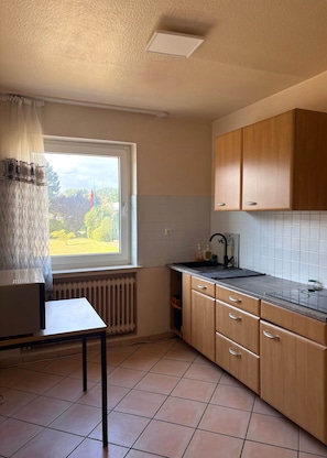 A kitchen with a window, a radiator, and wooden cabinets. - Spacious housing in a mixed-use area (Bielefeld)