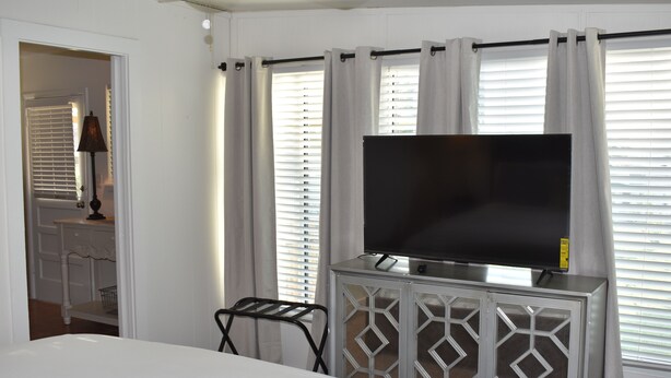 A hotel room with a bed, a TV on a cabinet, and a window with curtains. - La Ferme - french for country farmhouse 3BR/1BA in Rogers. (Rogers)