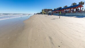 A wide sandy beach with a lifeguard tower and a covered pavilion.