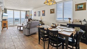 A spacious living room with a dining area, large windows, and a view of the ocean.
