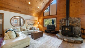 A cozy living room with a stone fireplace, wooden ceiling, and a large window.
