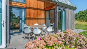 A modern house with a wooden exterior, large glass doors, and a patio with a table and chairs. - Stunning home in Kamperland with WiFi (Kamperland)