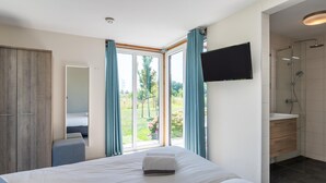 A hotel room with a bed, a TV mounted on the wall, a shower area, and a view of the outdoors. - Stunning home in Kamperland with WiFi (Kamperland)