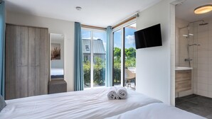 Une chambre d’hôtel moderne dotée d’un grand lit, d’un téléviseur fixé au mur et d’une salle de bain avec douche et toilettes.