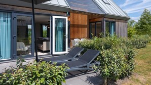 Une maison moderne dotée d’un patio comprenant deux fauteuils et un ensemble de mobilier de jardin pour prendre les repas.