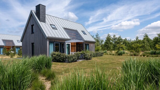 Une maison moderne avec un toit en pente, de grandes fenêtres et une pelouse bien entretenue.