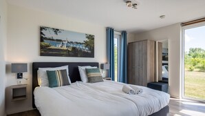 Une chambre moderne avec un grand lit, un tableau au-dessus du lit, une armoire et une vue sur l’extérieur.