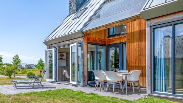 Une maison moderne dotée d’un patio comprenant une table et des chaises, une terrasse en bois et un toit en métal.