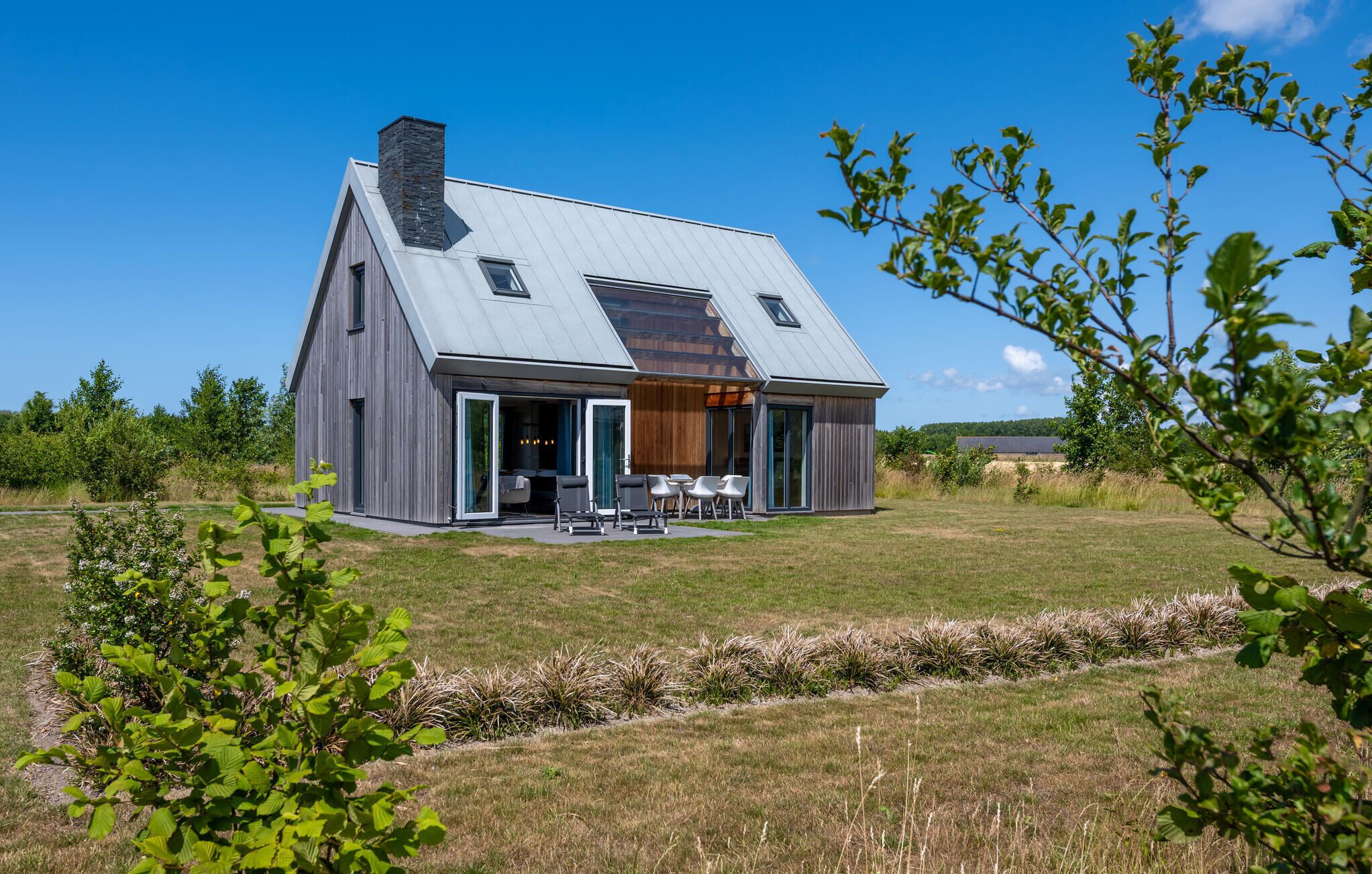 A modern house with a sloped roof, large windows, and a patio area with outdoor furniture.