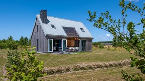 Une maison moderne dotée d’un toit en pente, de grandes fenêtres et d’un patio aménagé avec du mobilier d’extérieur.