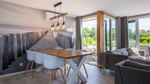A modern dining area with a wooden table and white chairs, a unique wall design, and a view of greenery through large windows. - 3 bedroom cozy home in Kamperland (Kamperland)