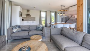 A modern living room with grey sofas, a wooden coffee table, and a dining area with white chairs. - 3 bedroom cozy home in Kamperland (Kamperland)