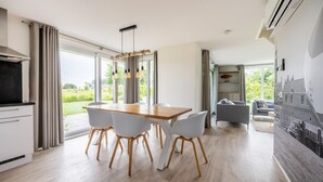 A modern kitchen with a wooden table and white chairs, large windows, and a view of greenery outside. - Gorgeous home in Kamperland with WiFi (Kamperland)