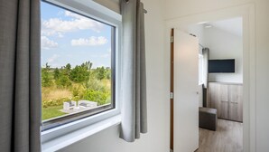 A room with a large window, grey curtains, a flat-screen TV mounted on the wall, and a wooden cabinet. - 3 bedroom awesome home in Kamperland (Kamperland)