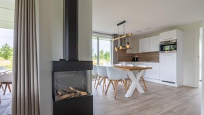 A modern kitchen with white cabinets, a wooden dining table, and a built-in fireplace. - 3 bedroom awesome home in Kamperland (Kamperland)