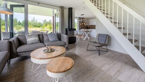 A modern living room with a sofa, two wooden coffee tables, a fireplace, and a staircase. - 3 bedroom awesome home in Kamperland (Kamperland)