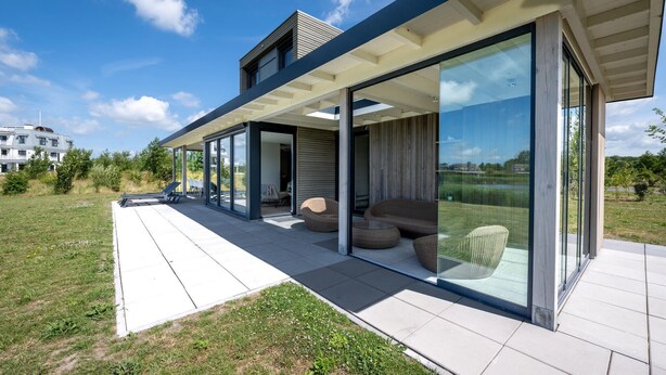 Et moderne hus med en overdækket terrasse, store skydedøre og udendørs møbler.