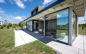 A modern house with a covered patio, large sliding glass doors, and outdoor seating. - Pet friendly home in Kamperland with WiFi (Kamperland)