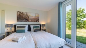 A bedroom with a large bed, two bedside tables with lamps, a painting on the wall, and a sliding glass door to a garden. - Amazing home in Kamperland with WiFi (Kamperland)