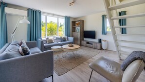 A modern living room with a sofa, coffee table, and TV, large windows with curtains, and a staircase. - Amazing home in Kamperland with WiFi (Kamperland)