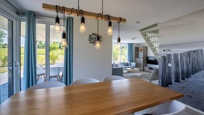 A modern dining area with a wooden table and white chairs, a kitchen in the background, and a view of the outdoors. - Amazing home in Kamperland with WiFi (Kamperland)