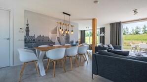 A modern kitchen with a dining area, a grey sofa, and a large window with a view of greenery. - 4 bedroom stunning home in Kamperland (Kamperland)