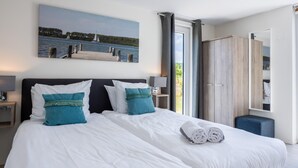 A hotel room with a large bed, a painting of a lake, a wardrobe, and a bathroom with a shower curtain. - 4 bedroom stunning home in Kamperland (Kamperland)