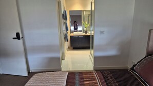 Une chambre avec un lit, une salle de bain avec une douche et un coin cuisine visible à travers une porte ouverte.
