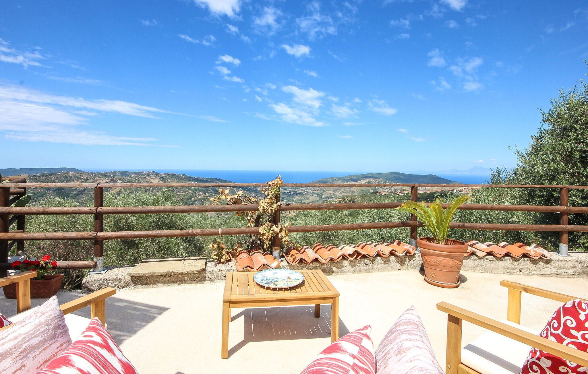 Una terraza con mesa y sillas de madera, vistas al campo y macetas de terracota.