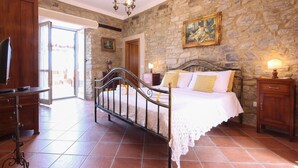 A bedroom with a stone wall, a bed with a metal frame, a wooden cabinet, and a television on a stand. - Nice home in Laureana Cilento (Laureana Cilento)
