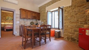 A kitchen with a stone wall, wooden cabinets, a dining table with chairs, a red refrigerator, and a window with curtains. - Nice home in Laureana Cilento (Laureana Cilento)