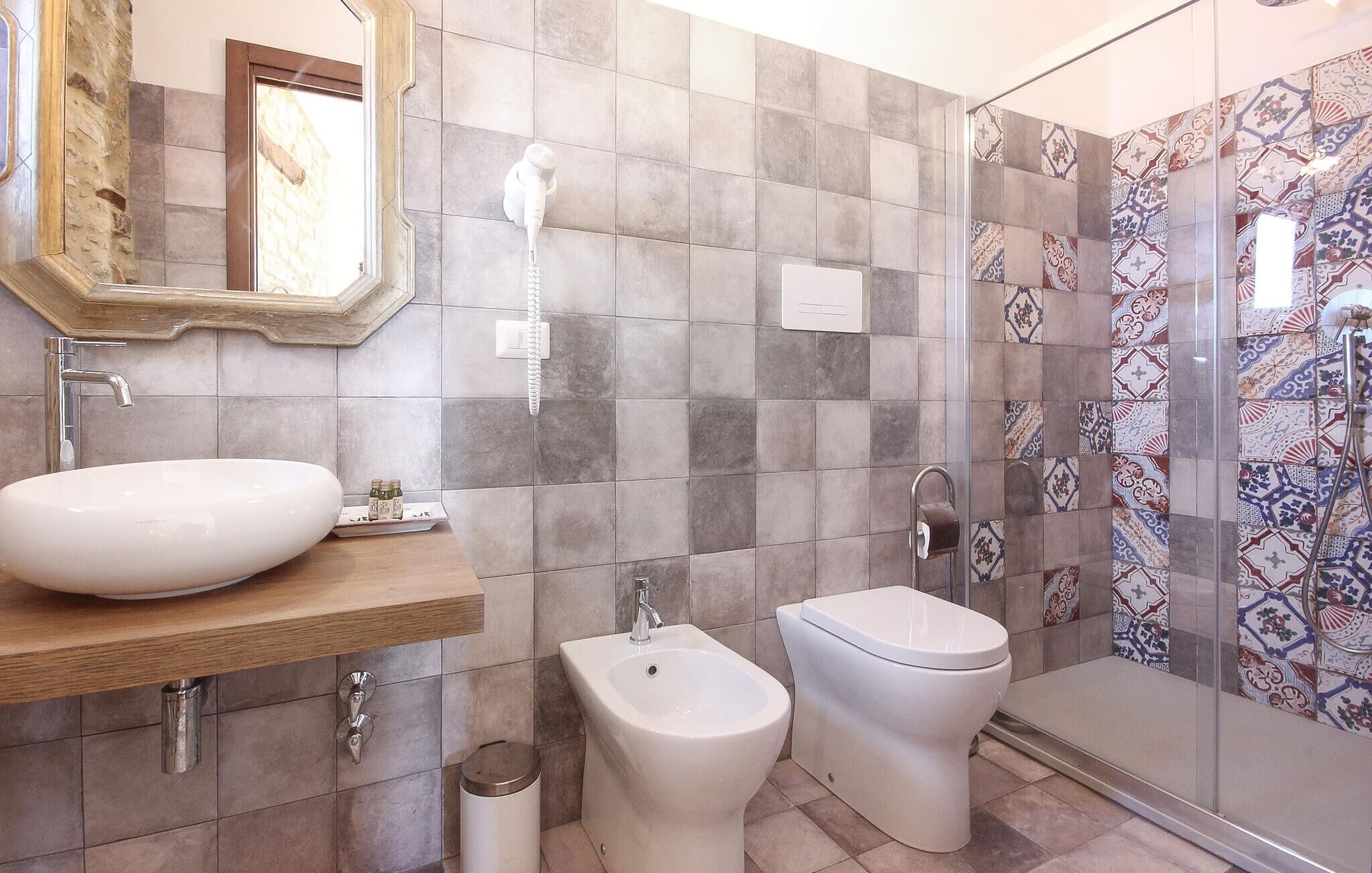 A bathroom with a large sink, bidet, toilet, and a shower with patterned tiles.