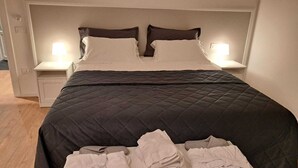 Ein ordentlich bezogenes Bett mit dunkler Decke und zwei Kissen, begleitet von Nachttischen mit Lampen.