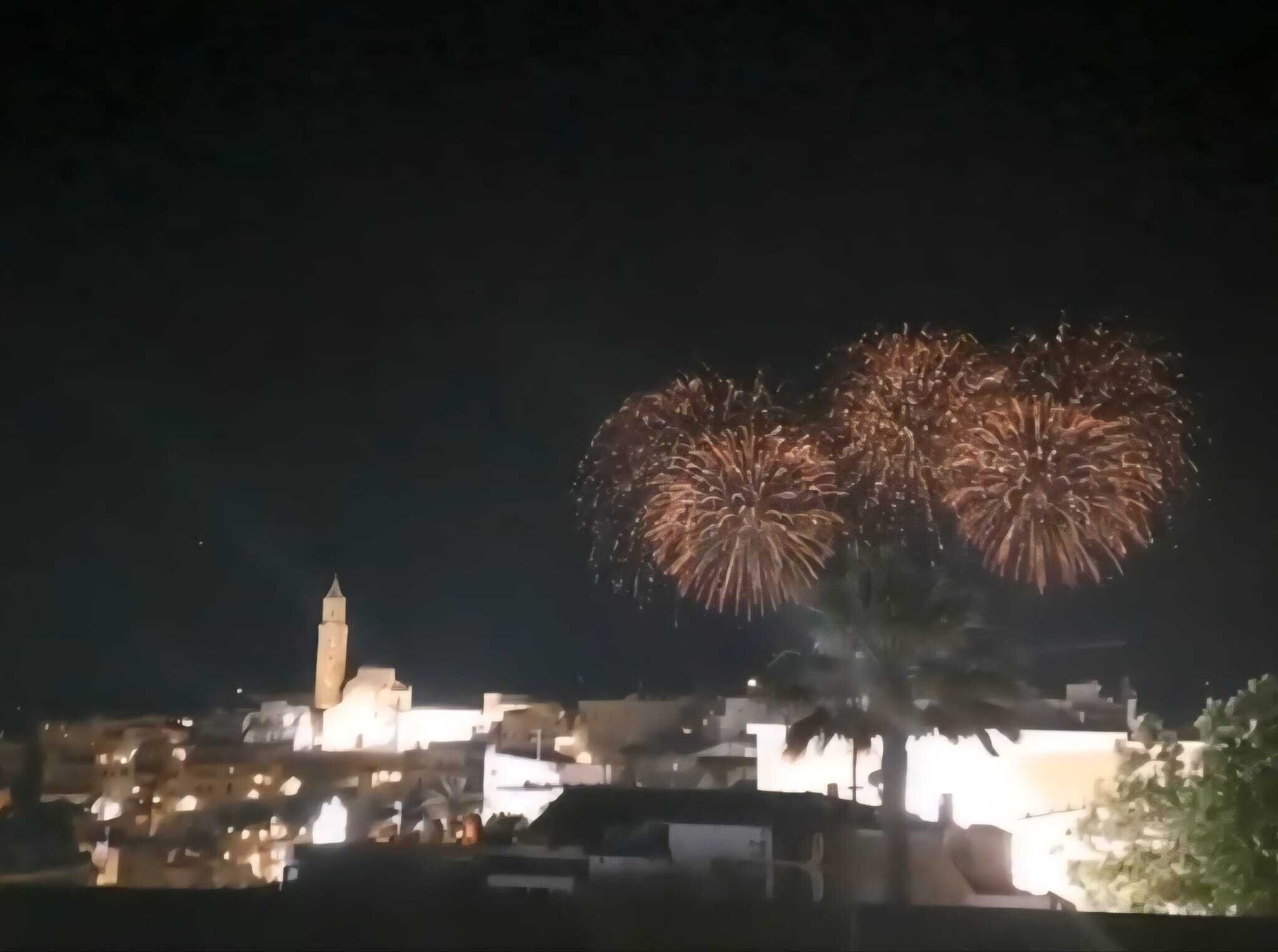 A night scene with fireworks over a cityscape, including a prominent tower and illuminated buildings.