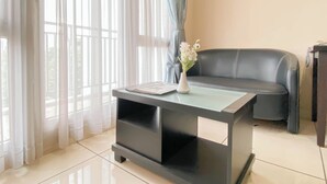 A modern living room with a black sofa, a glass coffee table, and sheer curtains. - Cozy Stay 1Br Apartment At 1 Cik Ditiro Residence (Jakarta)
