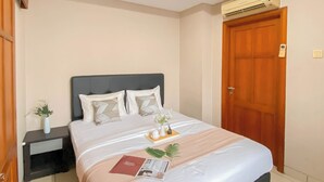 A hotel room with a bed, a nightstand, a wooden door, and an air conditioning unit. - Cozy Stay 1Br Apartment At 1 Cik Ditiro Residence (Jakarta)