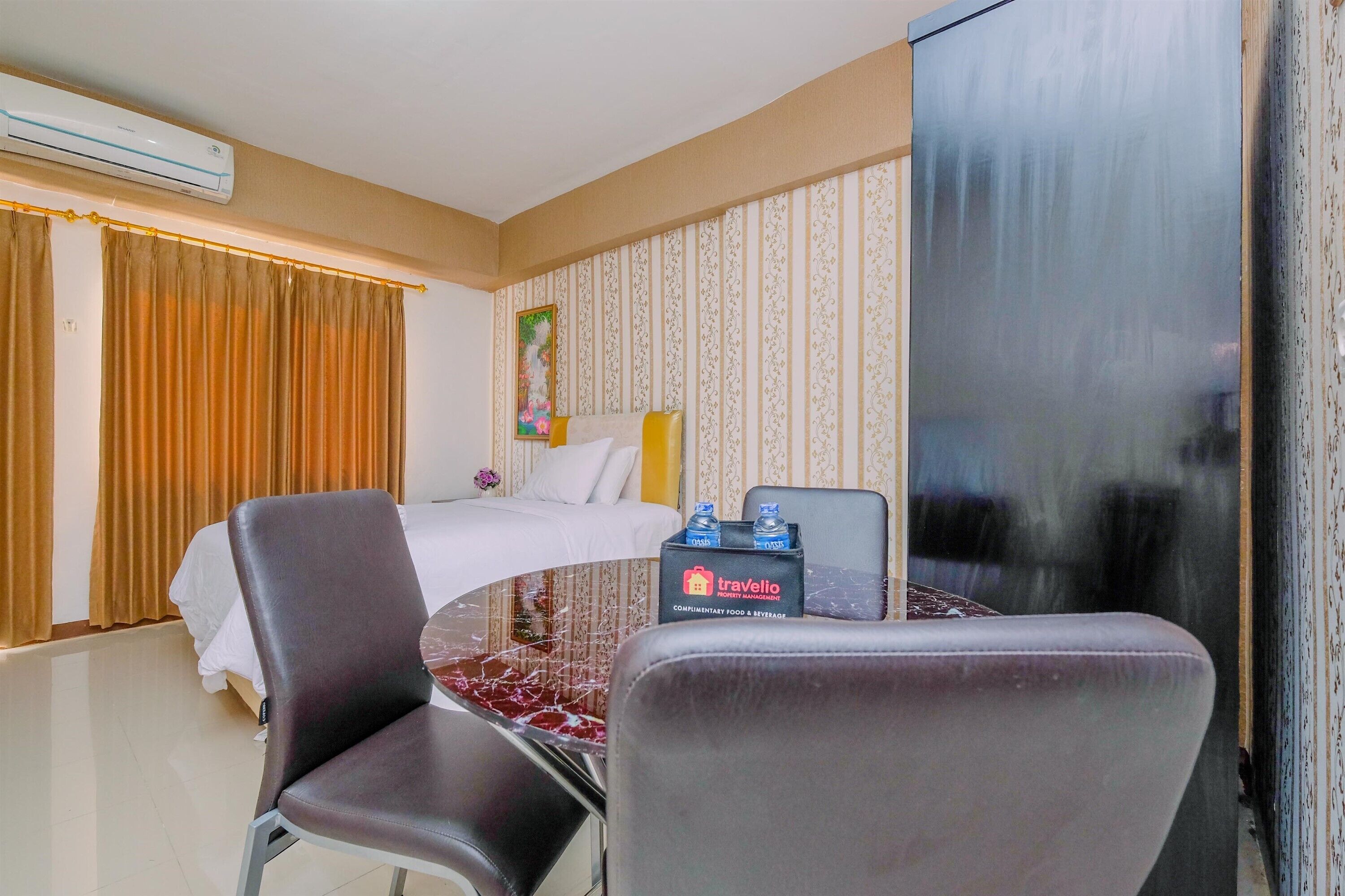 A hotel room with a bed, a desk with chairs, a minibar, and a large window with curtains.