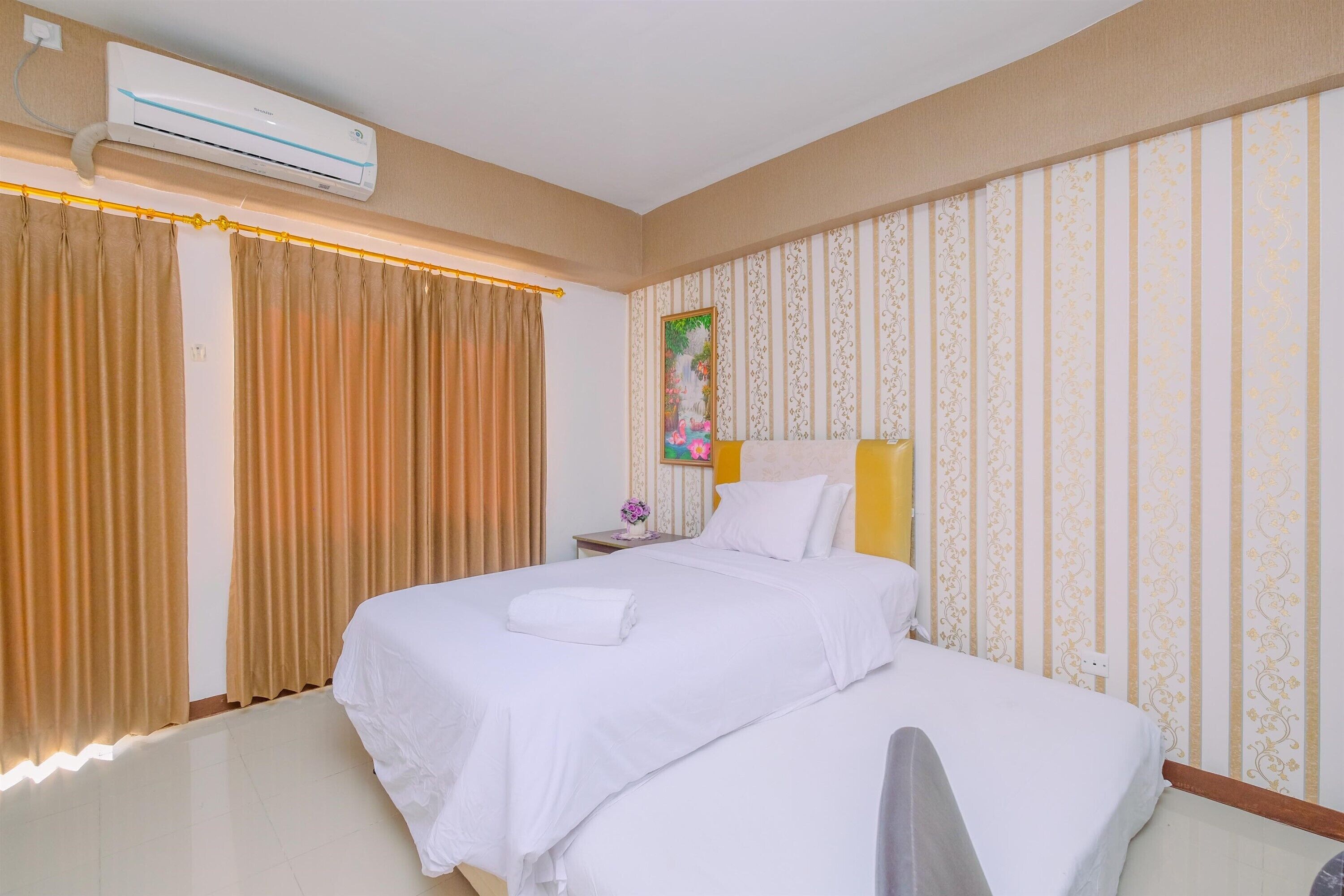 A hotel room with a bed, curtains, an air conditioning unit, a nightstand, and a wall with patterned wallpaper.