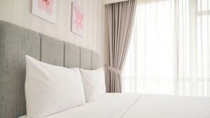 A neatly made bed with white linens and pillows, a grey upholstered headboard, and a window with sheer curtains. - Best Price And Elegant 2Br At Menteng Park Apartment (Jakarta)