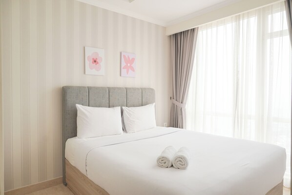 A neatly made bed with white linens and rolled towels, a grey upholstered headboard, and two floral wall art pieces. - Best Price And Elegant 2Br At Menteng Park Apartment (Jakarta)