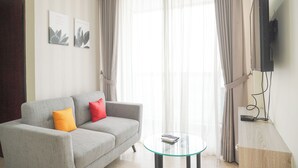 A living room with a grey sofa, orange and red cushions, a glass coffee table, and a TV mounted on the wall. - Best Price And Elegant 2Br At Menteng Park Apartment (Jakarta)
